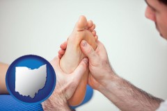 a podiatrist practicing reflexology on a human foot - with OH icon